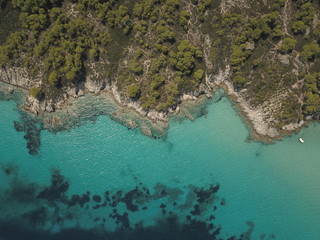 Fototapeta na wymiar Aerial view of small beach with turquoise water next to rocks and trees in the area of Agia Paraskevi Halkidiki, Greece. View from drone