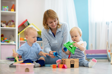 Teacher and one years old babies playing with educational toys in kindergarten
