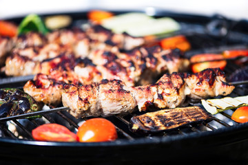 pieces of barbecue pork meat on a skewer with vegetables on the grill