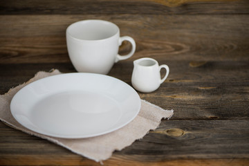 Obraz na płótnie Canvas empty white plate with cup and ceramic jug on old wooden background