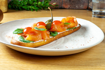Delicious and tasty Bruschetta with salmon, basil, cherry tomatoes and caper. Close up selective focus. Traditional italian cuisine appetizer. Seafood. Food photo for menu or recipe