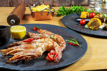 tasty and luxury food - grilled Langoustines on dark stone plate with sauce and lemon. Restaurant food styling. Delicious seafood on wooden background. lobster or big srhimp. Selective focus