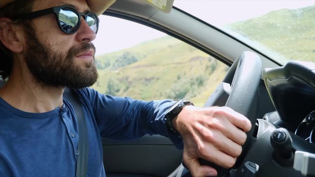 Portrait of bearded man driver tourist in hat. He is driving car and travelling through the amazing mountain valley and river, side view. Tourism and jeeping in mountains. Car trip on vacation.