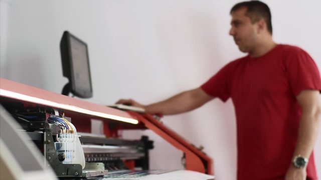 Operator works on computer by setting print options. Typography worker printing production on computerized modern printing press. Printmaker using ciss system for inkjet printer. Publishing industry.