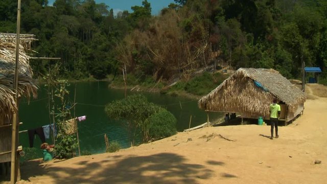 Wide high-angle sunny day still shot of an Aboriginal teenage boy walking at an indigenous village compound bordering Lake Temenggor, Malaysia