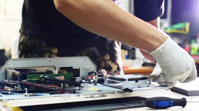 Computer hard drive ssd upgrade, diagnosing breakdowns. Technician detaches hard drive from monoblock repairing it in service center workshop, hands closeup. He unscrews computer details screwdriver.