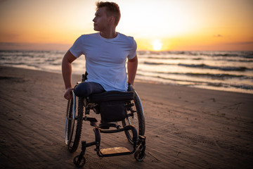 Handicapped man in wheelchair and his girlfriend alone on a beach at sunset