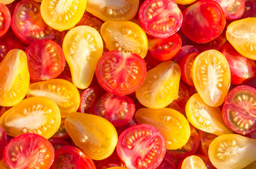 Fresh halves of Brazilian cherry tomatoes. Background of many colorful cherry tomatoes. Sliced yellow and red cherry tomatoes. Cherry tomatoes top view.