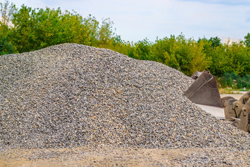 Yellow wheel loader bulldozer is working in quarry against the background of crushed stone storage.
