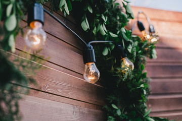 Garland with golden lights on green wreath on a wooden wall.