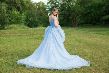 Fototapeta premium Woman with blond hair in a beautiful blue dress with a long sleeves outdoor. Romantic art photo