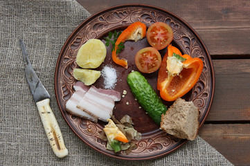 Boiled potatoes, tomato, lettuce, sprig of parsley and a strike knife in a brown ceramic plate on a background of coarse cloth