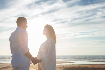 Love, waiting for the baby. Couple, pregnant woman and man, in white flying clothes, walk, hold hands, hug the tummy.