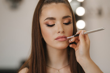 Makeup artist applies lipstick. Hand of make-up master, painting lips of young beauty redhead model. Make up in process. Closeup view