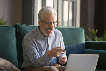 Happy old senior man laughing looking pointing at laptop screen