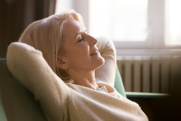 Happy lazy old woman relaxing meditating leaning on comfortable sofa