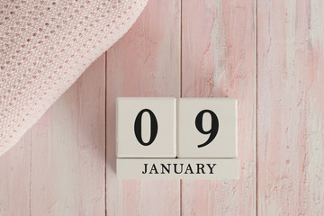 9 January Date on Cubes. Date on painted pink wood, next to baby blanket. Theme of baby due dates and birth dates.