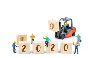 miniature worker team building standing front of forklift machine with white 2020 number on wooden block on white background, decoration to Happy new year 2020 concept.