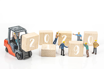 miniature worker team building standing front of forklift machine with white 2020 number on wooden block on white background, decoration to Happy new year 2020 concept.