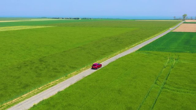 Aerial of a red car traveling through green fields of Normandy, France.