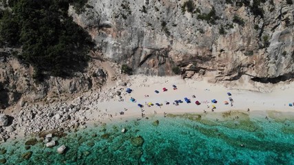 View from above, stunning aerial view of a beautiful beach full of beach umbrellas and people sunbathing and swimming on a turquoise water. Cala Gonone, Sardinia, Italy, Cala Mariolu