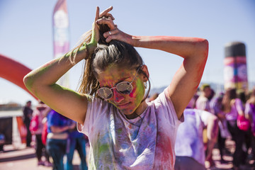 Young woman mess in holi color wearing sunglasses tying her hair outdoors