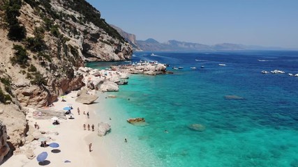 View from above, stunning aerial view of a beautiful beach full of beach umbrellas and people sunbathing and swimming on a turquoise water. Cala Gonone, Sardinia, Italy, Cala Mariolu