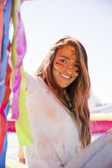 Portrait of a smiling young woman with painted face with holi color