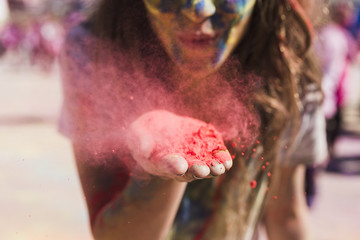 Young woman blowing the red holi color toward camera