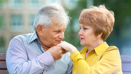 An old man kisses the hand of his wife. Lovers aged people are sitting on a bench, a man kisses a woman's hand.