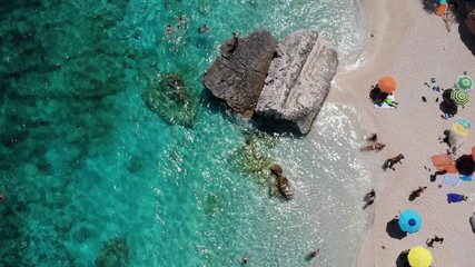 View from above, stunning aerial view of a beautiful beach full of beach umbrellas and people sunbathing and swimming on a turquoise water. Cala Gonone, Sardinia, Italy, Cala Mariolu