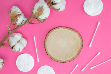 Cotton branch, pads and sticks, round wooden stand on bright pink background. Cosmetology, healthcare concept. Flat lay, top view, mock up, copy space, layout design