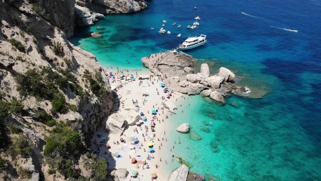 View from above, stunning aerial view of a beautiful beach full of beach umbrellas and people sunbathing and swimming on a turquoise water. Cala Gonone, Sardinia, Italy, Cala Mariolu