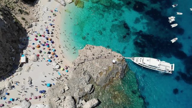 View from above, stunning aerial view of a beautiful beach full of beach umbrellas and people sunbathing and swimming on a turquoise water. Cala Gonone, Sardinia, Italy, Cala Mariolu