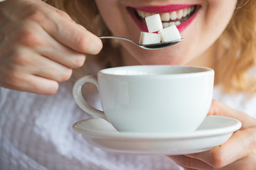 Sugar. Sweet. A woman holds sugar cubes on a spoon. Beautiful female mouth and calories concept....