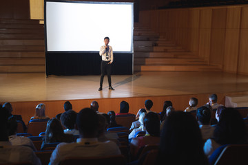 Businessman standing and giving presentation in auditorium 