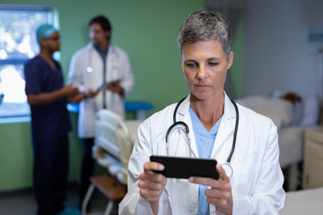 Matured female doctor using mobile phone in clinic at hospital