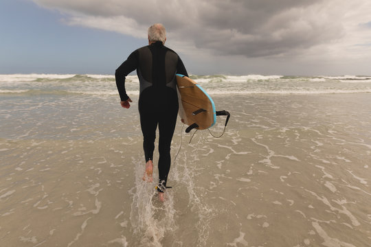 Senior man running with surfboard on the beach