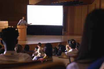Businessman standing around podium and giving presentation in the auditorium