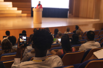 Man with smartphone taking video clip of businesswoman in the auditorium 