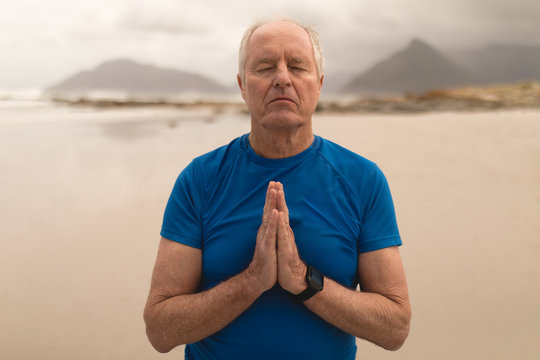 Senior man meditating in prayer position on the beach