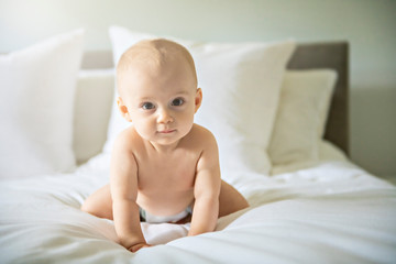 Cute happy baby girl in diaper on bed