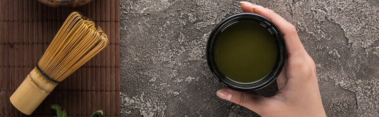 top view of woman holding matcha tea on table with whisk