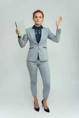 Full length studio portrait of a pretty young woman girl in a business suit on a white background with a folder in hands. He stands right in front of the camera, explains, with emotion.