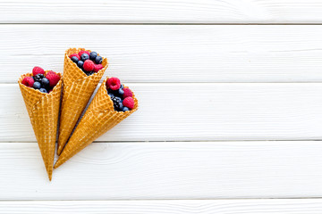 Summer breakfast with fresh berries in waffle cones on white wooden background top view mockup