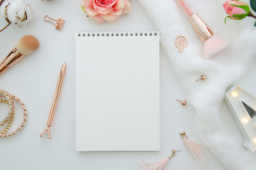 Flat lay mockup feminine desk workspace with spiral notebook, cosmetics and flowers on white...
