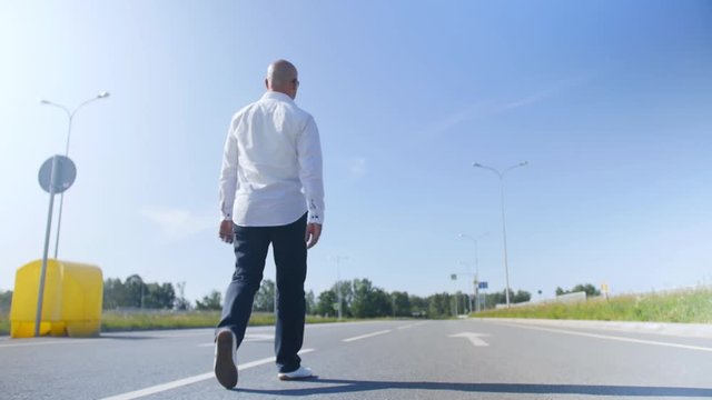 Rear view of a bald man walking along еmpty the road. Full shot.