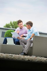 Two attractive business man sitting outdoors and discussing work whilst looking at laptop, they are casually dressed and culd be in a new start up business