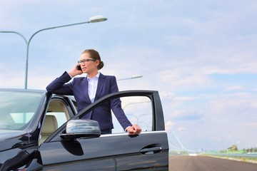 Businesswoman talking on smartphone while standing by car on road