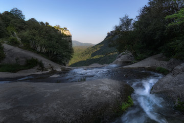Fototapeta na wymiar River running between rocks, trees & far mountains